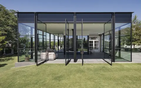 Concept visual of Glasshus: a black-framed glass pavilion with a thin flat roof on a green lawn