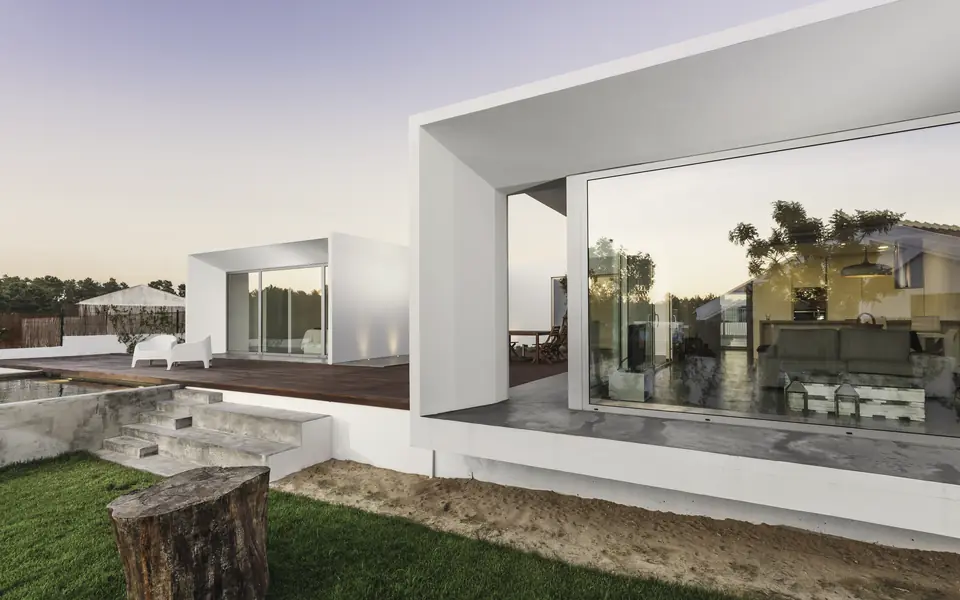Ramme concept visual: a white minimalist house with a deep rectangular frame around a glazed living room, in warm evening light